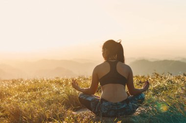 Genç bir atletik kadın gün batımında dışarıda meditasyon yapıyor.