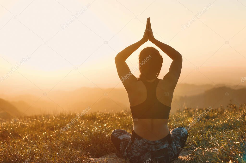 A back view of woman that practices yoga in nature. Lotus pose with her hands over her head