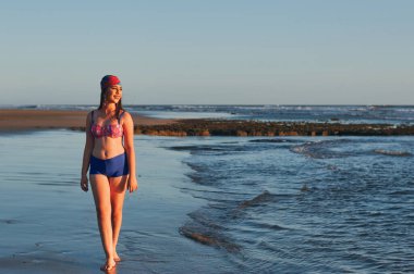 Mayolu mutlu bir kadın deniz kıyısında yürüyor ve başka tarafa bakıyor.