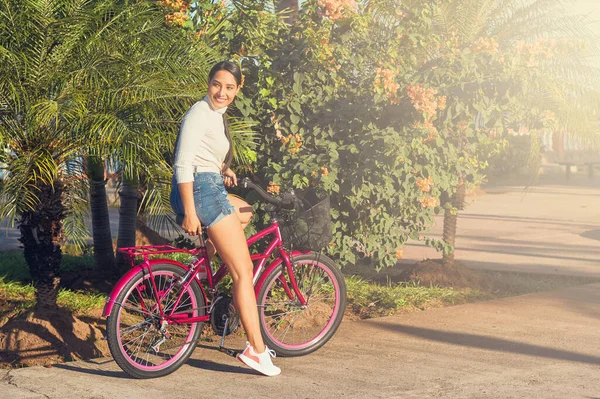 Güneşli bir günde bisiklet süren ve gülümseyen Latin bir kızın portresi.
