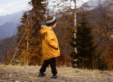 Parlak sarı ceketli bir çocuk dağlarda yürüyor. Bir çocukla seyahat etmek. Sağlıklı dağ havası.