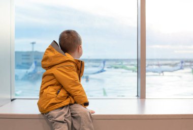 Havaalanındaki büyük pencerede sarı ceketli bir çocuk..