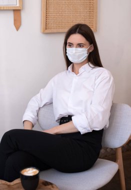 Bir kafede tıbbi maske takan genç bir kadın..
