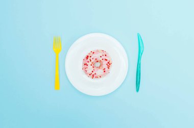 Mavi bir tabakta, çatal bıçaklı pembe çörek..