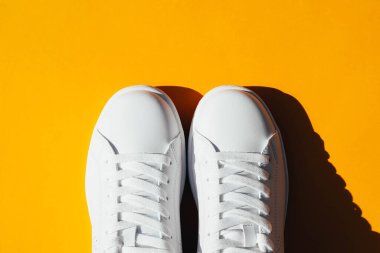 Turuncu arka planda sert gölgeli beyaz spor ayakkabılar..