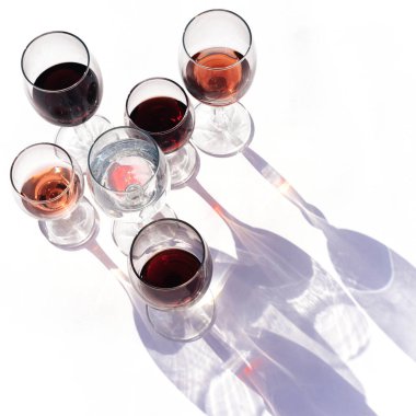 Beyaz arka planda farklı türde bardaklarda şarap. Gözlükten yapılmış şık sert gölgeler.