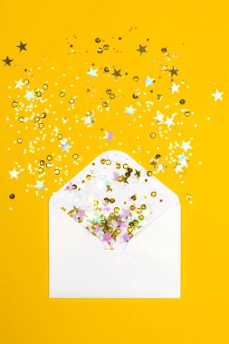 Sarı arka planda zarftan yayılmış köpüklü konfeti..