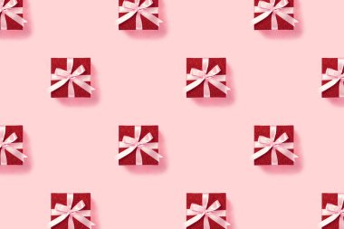 Pembe arka planda pembe kurdeleli kırmızı hediye kutusu.
