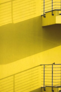 Gölgeli balkonlu sarı duvar.