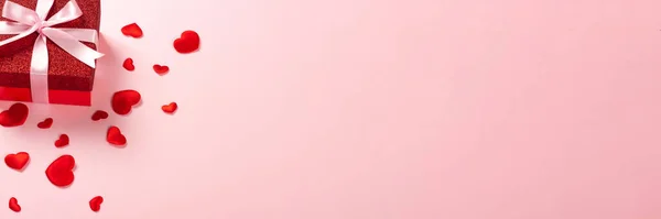 Pembe arka planda pembe kurdeleli kırmızı hediye kutusu.