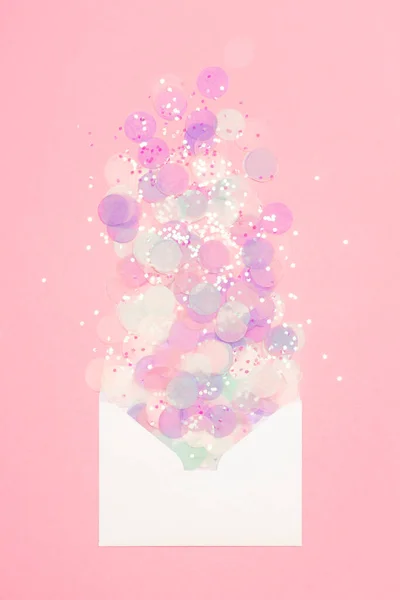 Espumante confete espalhado do envelope no fundo rosa pastel. — Fotografia de Stock