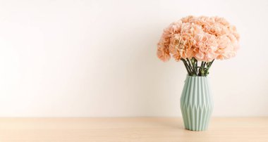 Açık yeşil seramik vazoda bej karanfil açık ahşap masa üzerinde.