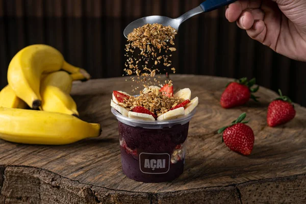 Lezzetli Brezilya Acai Kreması, çilekli, muzlu ve tahıllı bir fincanda, ahşap bir arka planda. Yaz acai smoothie