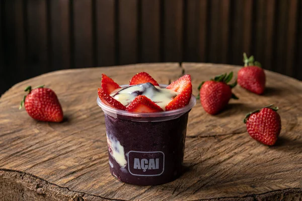Lezzetli Brezilya Acai Kreması, çilekli, muzlu ve tahıllı bir fincanda, ahşap bir arka planda. Yaz acai smoothie