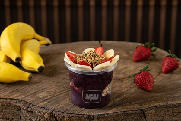 Lezzetli Brezilya Acai Kreması, çilekli, muzlu ve tahıllı bir fincanda, ahşap bir arka planda. Yaz acai smoothie