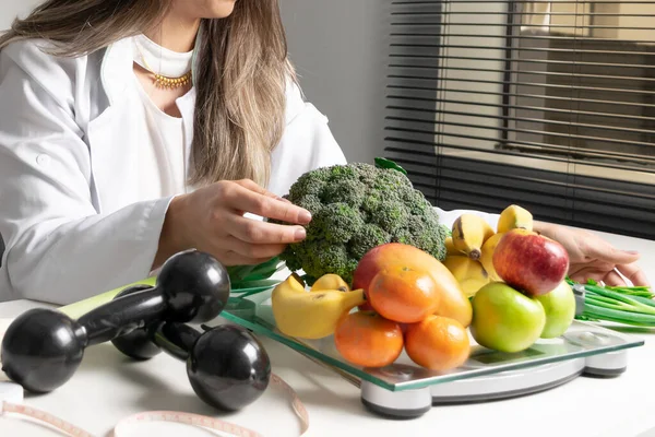 Female nutritionist in her office,  showing healthy vegetables and fruits. Healthcare and diet concept. Lifestyle.