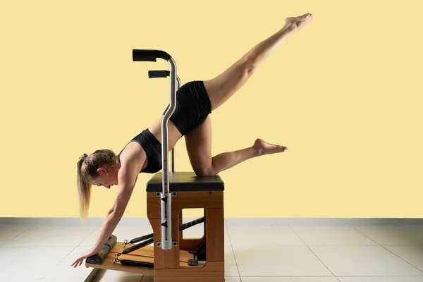 Woman doing pilates exercises in a chair equipment, yellow backgound