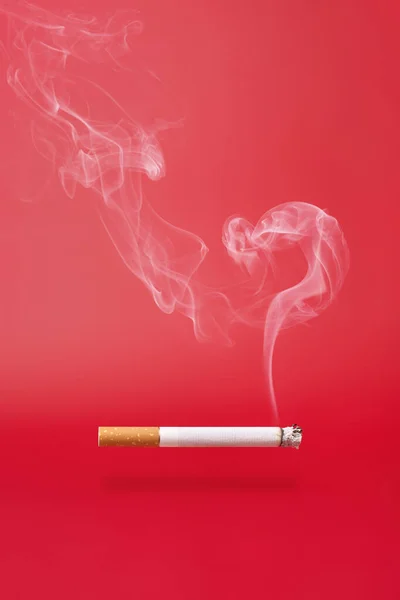 Rauch als Fragezeichen und eine rauchende Zigarette auf rotem Hintergrund. — Stockfoto