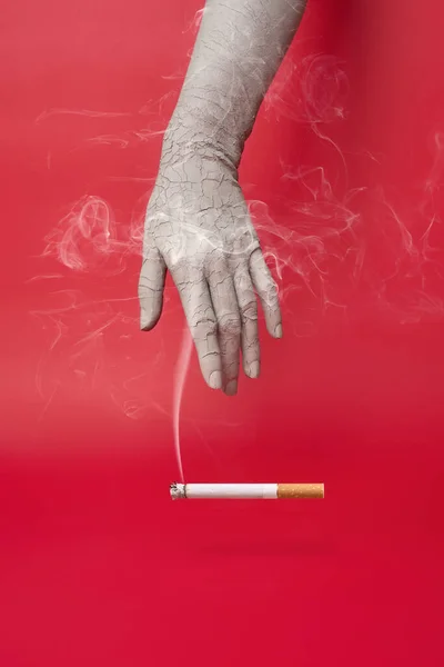 Trockene und rissige Hand und eine rauchende Zigarette auf rotem Hintergrund. — Stockfoto