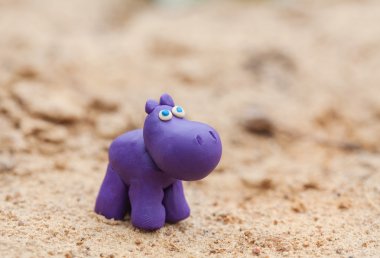 Plasticine world - little homemade purple hippo on a sand backgr
