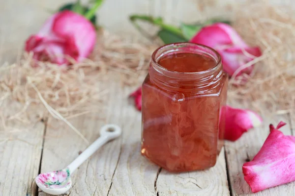 Jar of rose petal jam on a wooden table with flowers roses, sele