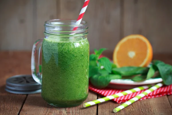Healthy green smoothie made from spinach, kiwi, bananas and oranges in a jar with red straw on a wooden table, selective focus