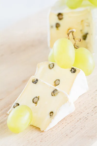 Dos trozos de Brie con pimienta verde y uvas —  Fotos de Stock