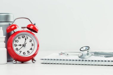 Tıbbi ya da sağlık konsepti afişi. Üzerinde steteskop olan kırmızı alarm saati spiral not defteri ve haplar, sprey. Tıbbi çalışma ya da araştırma, evrak kontrolü. Doktor randevusu. Boşluğu kopyala.
