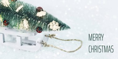 Mutlu Noeller tebrik kartı mesajları. Süslü oyuncak Noel ağacı, kar üzerinde beyaz kızakla bokeh ışıkları. Asgari