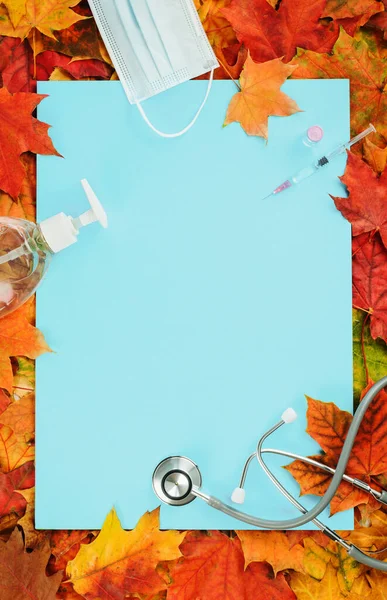 Flu and cold season frame on blue with fall leaves. Flu season or second wave. Face protective mask, sanitizer or soap and flu jab vial. Vaccine trial vaccination and immunization concept poster