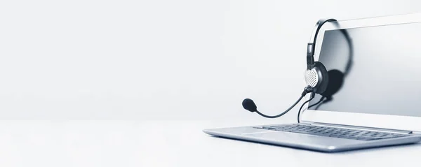 Dizüstü bilgisayar. Model ekran ve kulaklıklar gri masada ve arka planda geniş pankart. Uzaktan öğrenme ya da evden çalışma, çevrimiçi kurslar veya asgari konsepti destekleme. Yardım masası veya çağrı merkezi kulaklığı