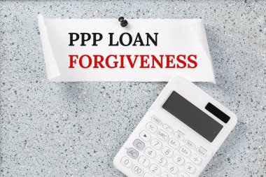 Gri tıpa uyarı panosunda hesap makinesiyle PPP Loan Af Yazısı. Küçük işletme maaş koruma programı. Bankacılık ve finans kavramı