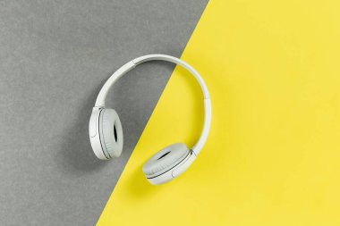Aydınlatıcı sarı ve gri arka planda kablosuz, modern gri kulaklıklar. Uzaktan öğrenme, müzik veya radyo dinleme. Kopya alanı ile trend yaşam tarzı kavramı
