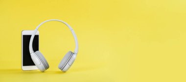 Sarı arkaplanı aydınlatan cep telefonlu kablosuz gri kulaklıklar