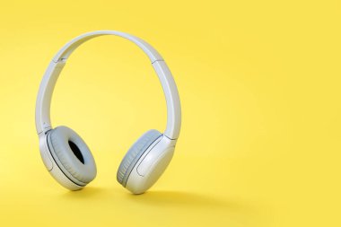 Kablosuz, modern, gri kulaklıklar sarı arka planda dikiliyor. Aydınlatıcı. Uzaktan öğrenme, müzik veya radyo dinleme. Boşluğu kopyala