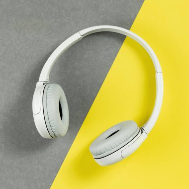 Aydınlatıcı sarı ve gri arka planda kablosuz, modern gri kulaklıklar. Uzaktan öğrenme, müzik veya radyo dinleme. Kopya alanı ile trend yaşam tarzı kavramı
