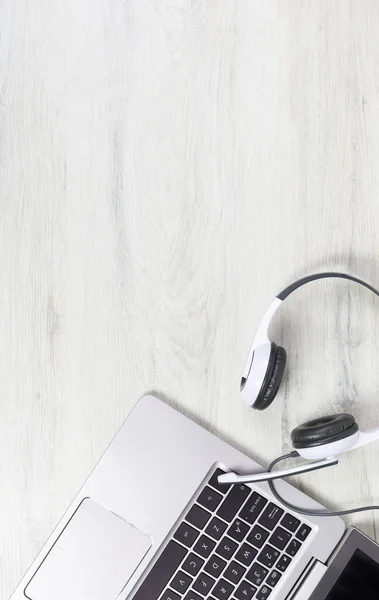 Dizüstü bilgisayar. Gri masadaki klavye ve kulaklıklar ve sade ahşap arka plan afişi. Yardım masası ya da çağrı merkezi kulaklığı. Uzak öğrenim veya evden çalışma, çevrimiçi kurslar veya destek merkezi konsepti.