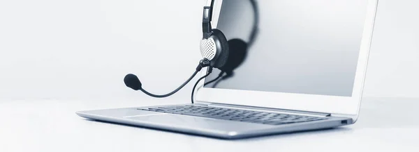Dizüstü bilgisayar. Model ekran ve kulaklıklar gri masada ve arka planda geniş pankart. Uzaktan öğrenme ya da evden çalışma, çevrimiçi kurslar veya asgari konsepti destekleme. Yardım masası veya çağrı merkezi kulaklığı