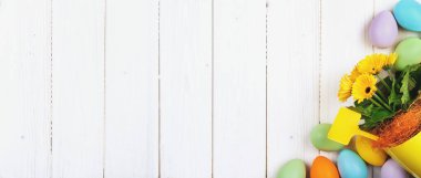 Ahşap zemin üzerinde birkaç parlak renkli paskalya yumurtası fotokopi alanı ile düzleştirilmiş. Mutlu Paskalyalar için minimum konsept kart ya da afiş sınırı. Saksı bahar çiçekleri