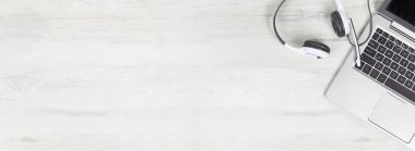 Dizüstü bilgisayar. Gri masadaki klavye ve kulaklıklar ve sade ahşap arka plan afişi. Yardım masası ya da çağrı merkezi kulaklığı. Uzak öğrenim veya evden çalışma, çevrimiçi kurslar veya destek merkezi konsepti.