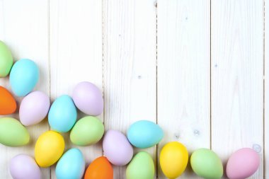 Ahşap zemin üzerinde birkaç parlak renkli paskalya yumurtası fotokopi alanı ile düzleştirilmiş. Mutlu Paskalyalar için Asgari Konsept Kart veya Pankart Sınırı