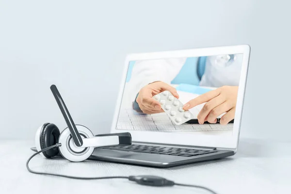 Doktorlar dizüstü bilgisayarlardaki haplara el işaretleriyle bakıyor. Masasında kulaklık olan bir dizüstü bilgisayar. Uzaktan öğrenme ya da evden çalışma, internet kursları ya da teletıp denilen video konsepti. Online doktor randevusu