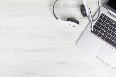 Dizüstü bilgisayar. Gri masadaki klavye ve kulaklıklar ve sade ahşap arka plan afişi. Yardım masası ya da çağrı merkezi kulaklığı. Uzak öğrenim veya evden çalışma, çevrimiçi kurslar veya destek merkezi konsepti.