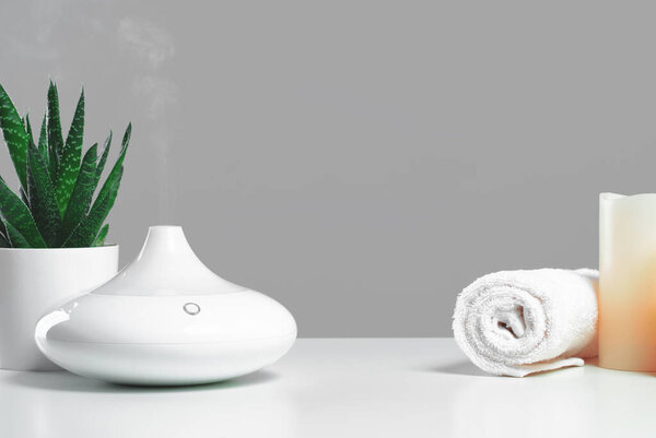 Aroma oil diffuser and candles with white towel on table. Spa, relaxation aromatherapy or yoga studio concept. Copy space