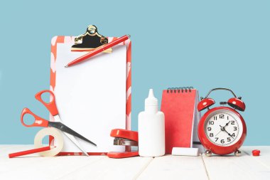 Masa mavi arka planda ofis ve okul kırmızı kırtasiyesi grubu. Çalar saat. Okula dönüş afişi. Eğitim ve yaratıcılık zanaatı kavramı. Seçici odaklanma. Uzayı kopyala program uydurma not defteri