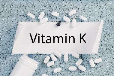 Not panosundaki K vitamini metni. Etrafa hap ve tabletler saçılmış.