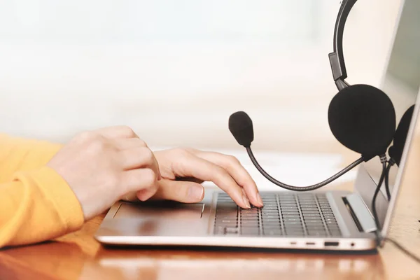 Dizüstü bilgisayar. Kulaklık ya da ahşap masa ve arka planda kulaklık. Dişi eller dizüstü bilgisayarın üzerinde. Uzaktan öğrenme ya da evden çalışma, çevrimiçi kurslar ya da destek kavramı. Yardım masası veya çağrı merkezi operatörü