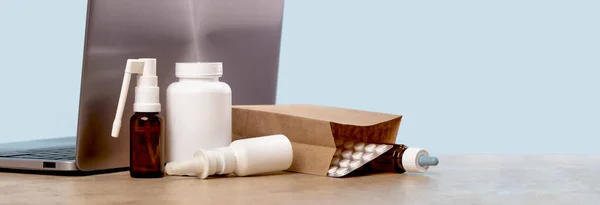 Online pharmacy. prescription drugs and over the counter medication ready for delivery to customers banner. Pills and spray white mockup containers in buff paper bags near laptop. Drugstore shopping
