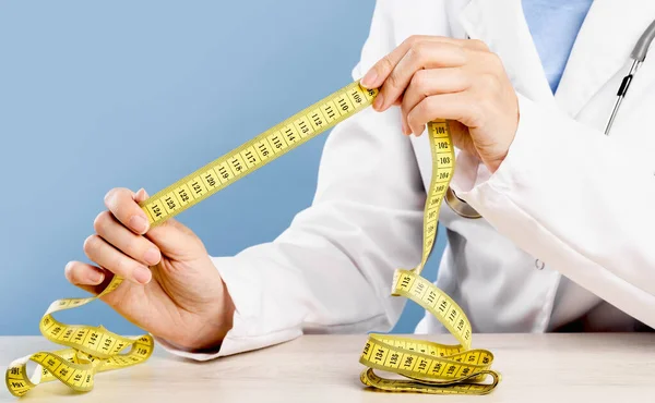 Doctor mid-section holding yellow tape measure. Obesity and diet concept. Weight management and checkups