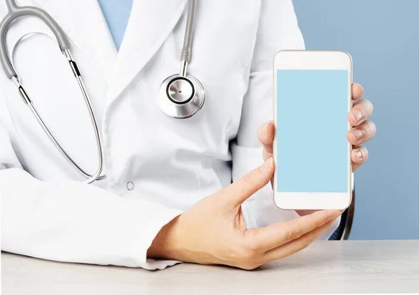 Kadın doktorun elinde tıbbi bir uygulama ile akıllı telefon tutarken çekilmiş görüntüsü. Metin için boş mavi kopya alanı. Çevrimiçi teletıp desteği veya danışma